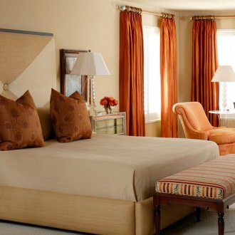 Πορτοκαλί κουρτίνες, πολυθρόνα και καναπές στο υπνοδωμάτιο