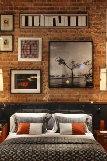 Πίνακες και φωτογραφίες σε έναν τοίχο από τούβλα στο εσωτερικό του υπνοδωματίου