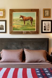 Ένας πίνακας με άλογο και άλλα έργα ζωγραφικής πάνω από το κεφάλι του κρεβατιού